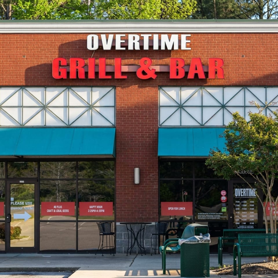 Exterior of Overtime Grill & Bar featuring a red brick facade, turquoise awnings, outdoor seating, benches, and trees.