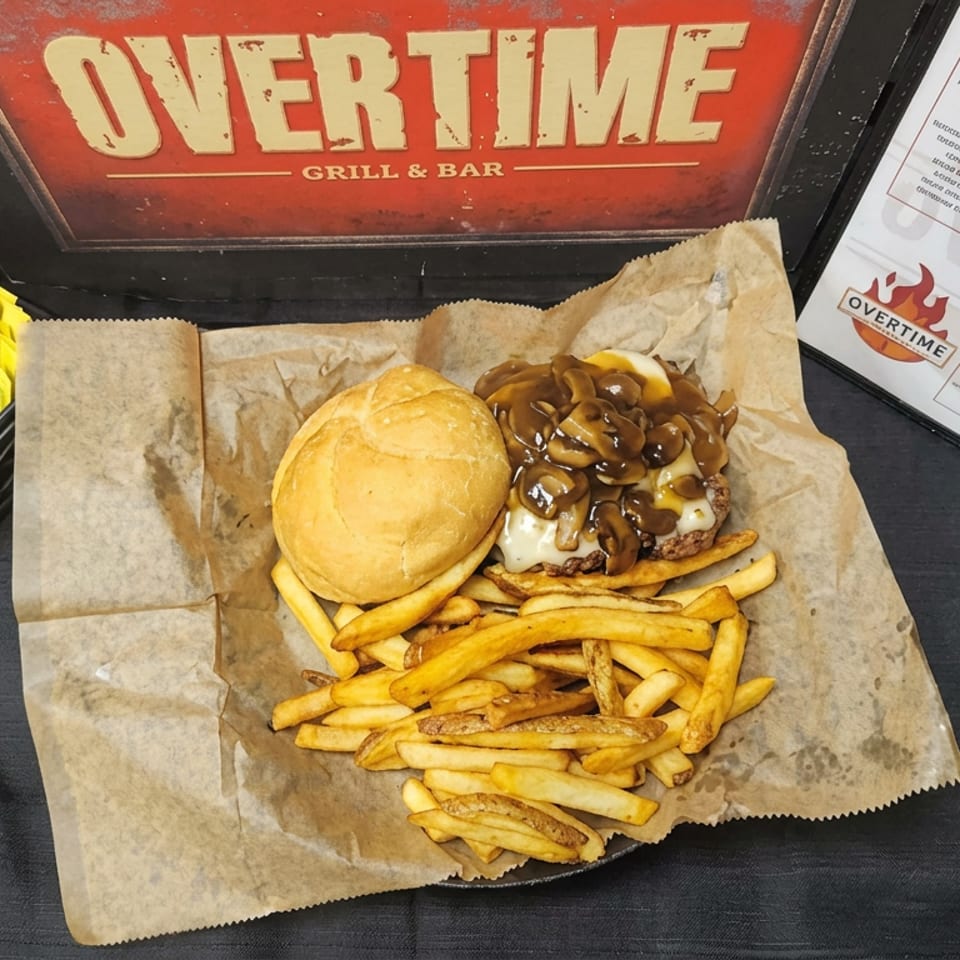 Mushroom cheeseburger with melted cheese and fries served on parchment at Overtime Grill & Bar.