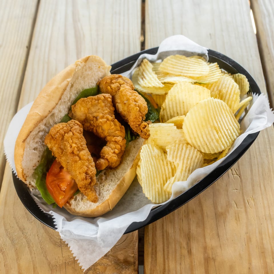 Crispy fried chicken sandwich with lettuce and tomato served alongside ridged potato chips in a black basket.