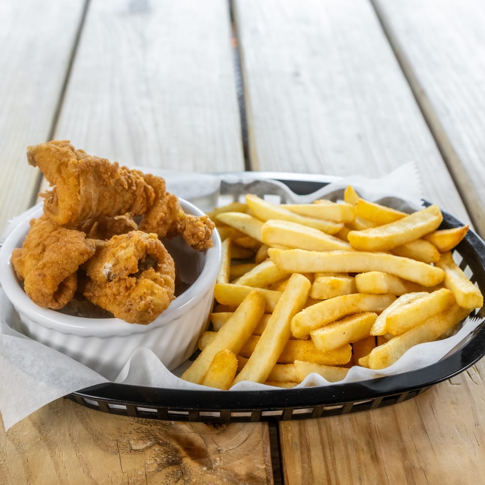 Basket of golden fried chicken tenders and thick-cut fries served on a wooden table.